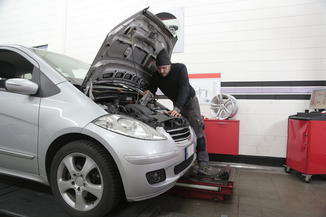 Car Mechanic Working Under The Hood Of A Silver Car